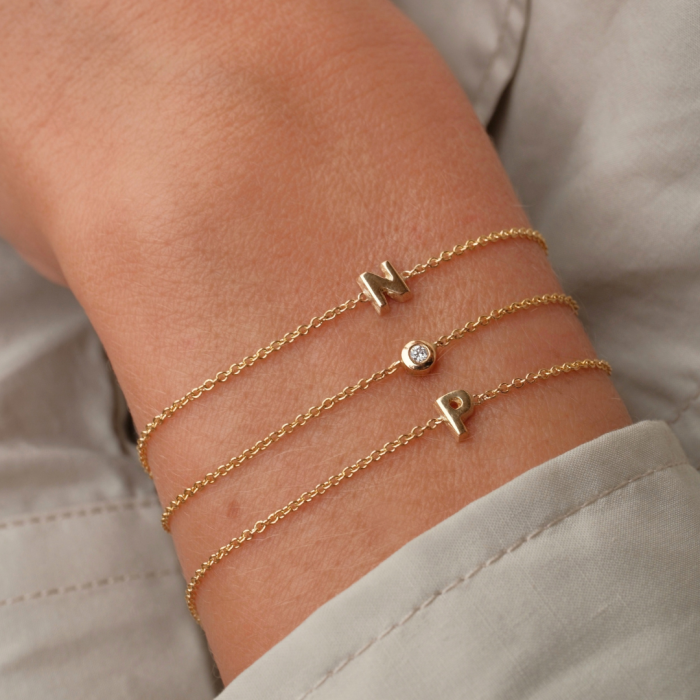Gouden Minitials armband met hangers en diamant gedragen om de pols