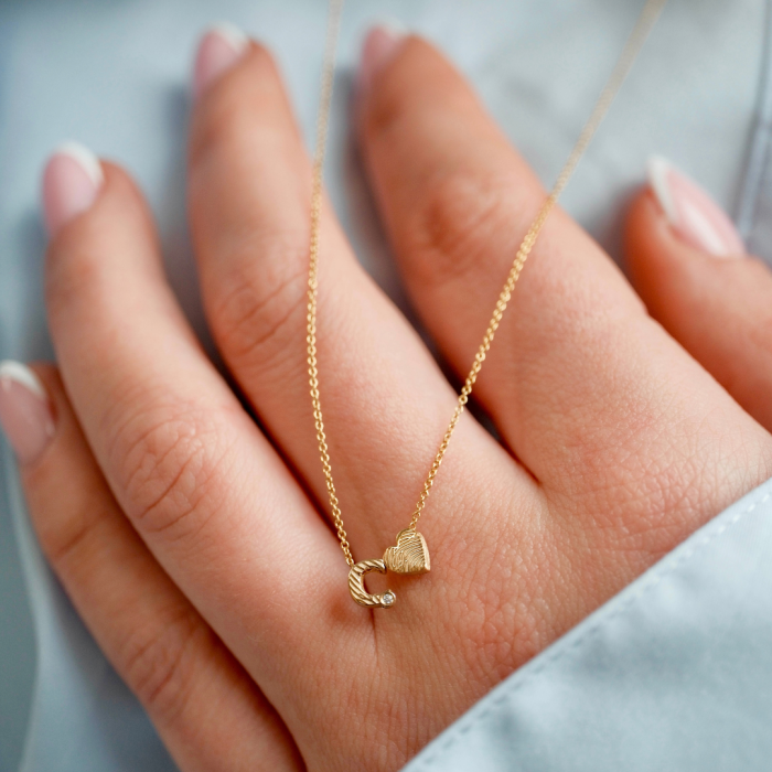 Gouden Minitials ketting met vingerafdrukhangers op een hand met lichtblauwe mouw